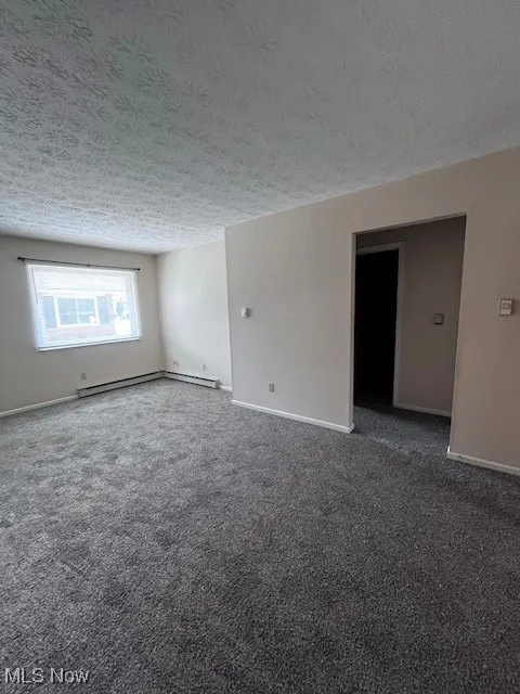 Carpeted empty room featuring a textured ceiling and baseboard heating