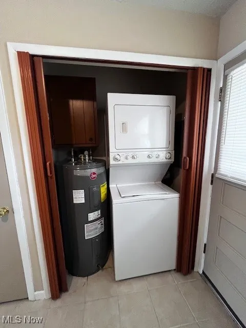 Washroom with estacked washer and dryer, light tile patterned flooring, and water heater