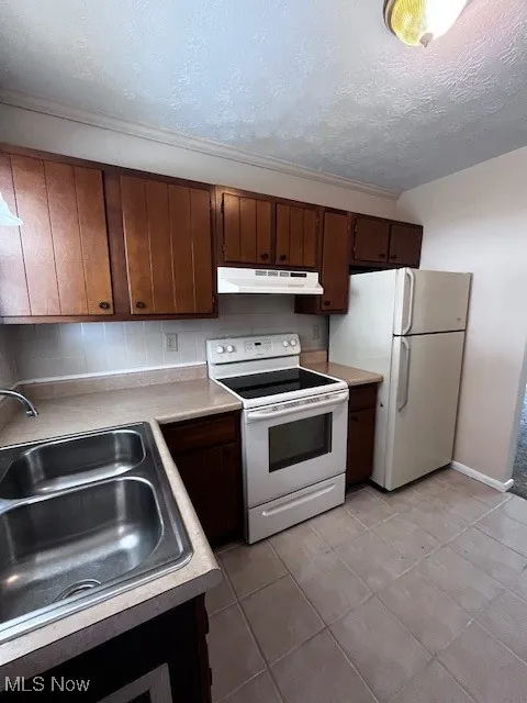 Kitchen with electric stove, a textured ceiling, refrigerator, light countertops, and ventilation hood