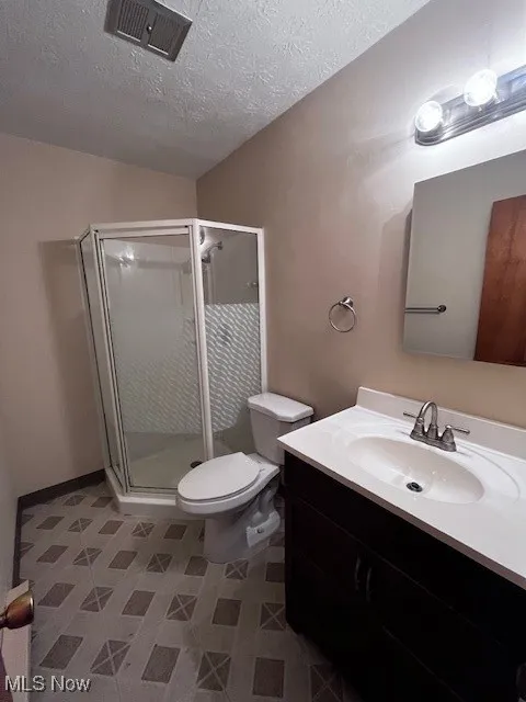 Full bath with a textured ceiling, vanity, and a shower stall