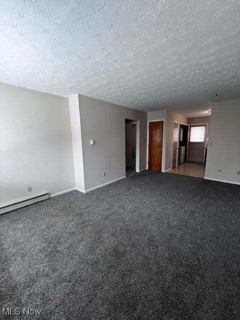 Carpeted empty room with a textured ceiling and baseboard heating