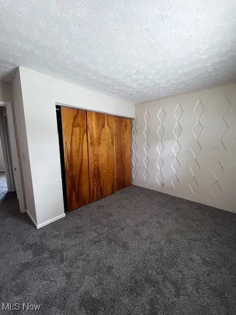Unfurnished bedroom with dark colored carpet, a textured ceiling, and a closet