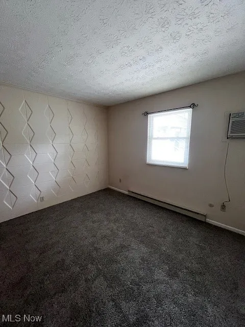 Empty room featuring a baseboard heating unit, a textured ceiling, and carpet