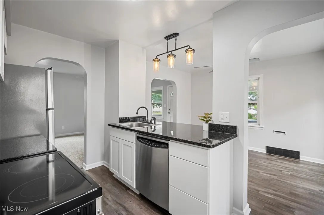 Kitchen with arched walkways, stainless steel appliances, dark wood-type flooring, white cabinets, and dark stone countertops