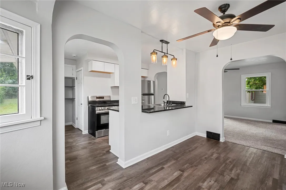 Kitchen with arched walkways, ceiling fan, appliances with stainless steel finishes, white cabinets, and dark wood-type flooring