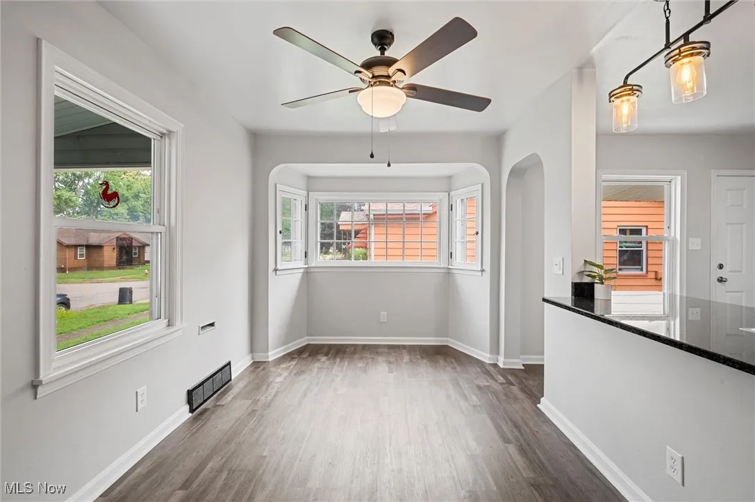 Unfurnished dining area featuring arched walkways, dark wood-style floors, and a ceiling fan