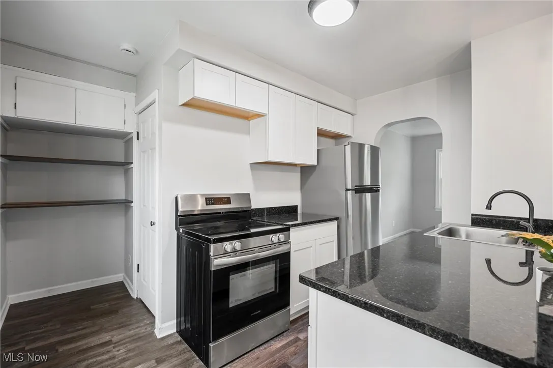 Kitchen featuring stainless steel appliances, arched walkways, dark wood-type flooring, white cabinets, and dark stone countertops