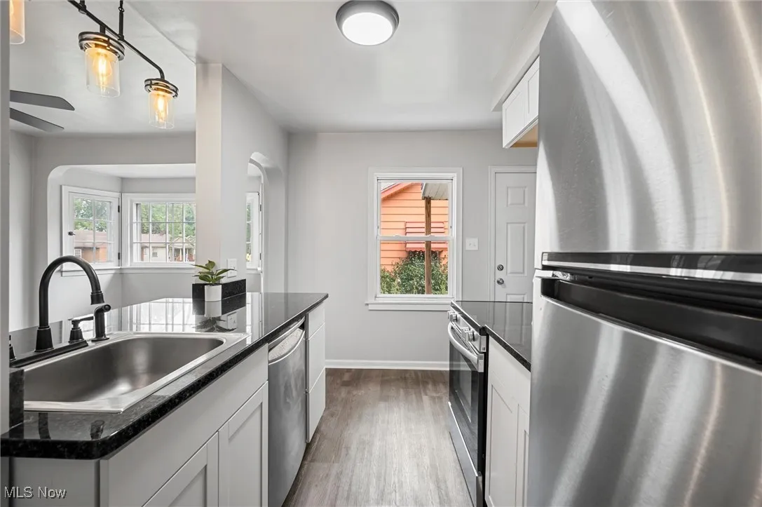 Kitchen with stainless steel appliances, dark wood-type flooring, arched walkways, white cabinetry, and dark stone countertops