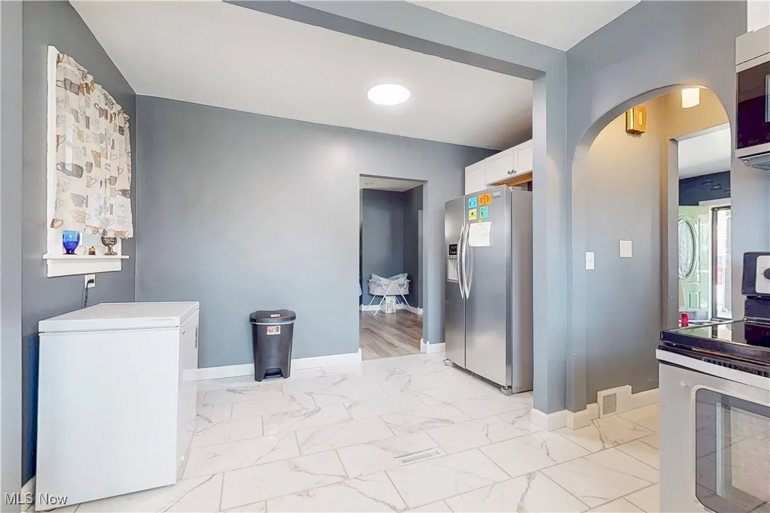 Kitchen with stainless steel appliances, light marble finish floors, arched walkways, and white cabinets