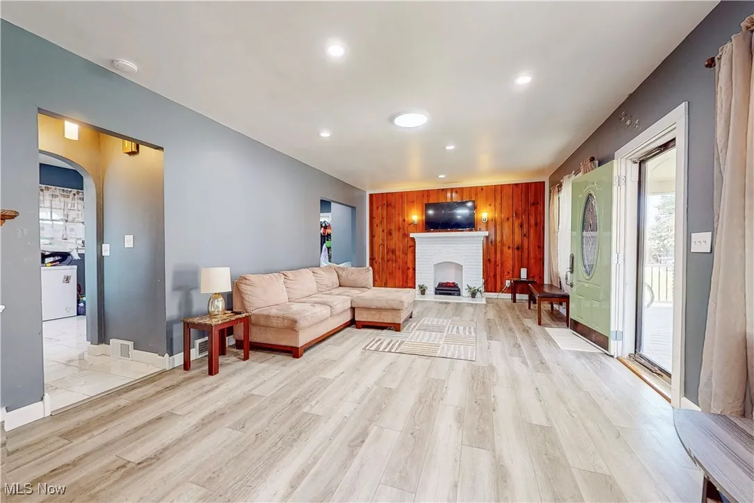 Living area with a fireplace, wooden walls, arched walkways, recessed lighting, and light wood-style flooring