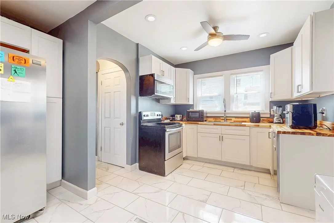 Kitchen with stainless steel appliances, a ceiling fan, butcher block countertops, light marble finish flooring, and white cabinets