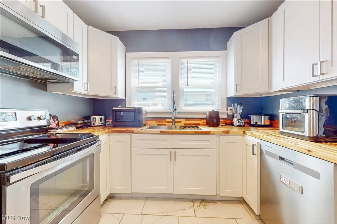 Kitchen with butcher block countertops, stainless steel appliances, white cabinets, and light marble finish floors