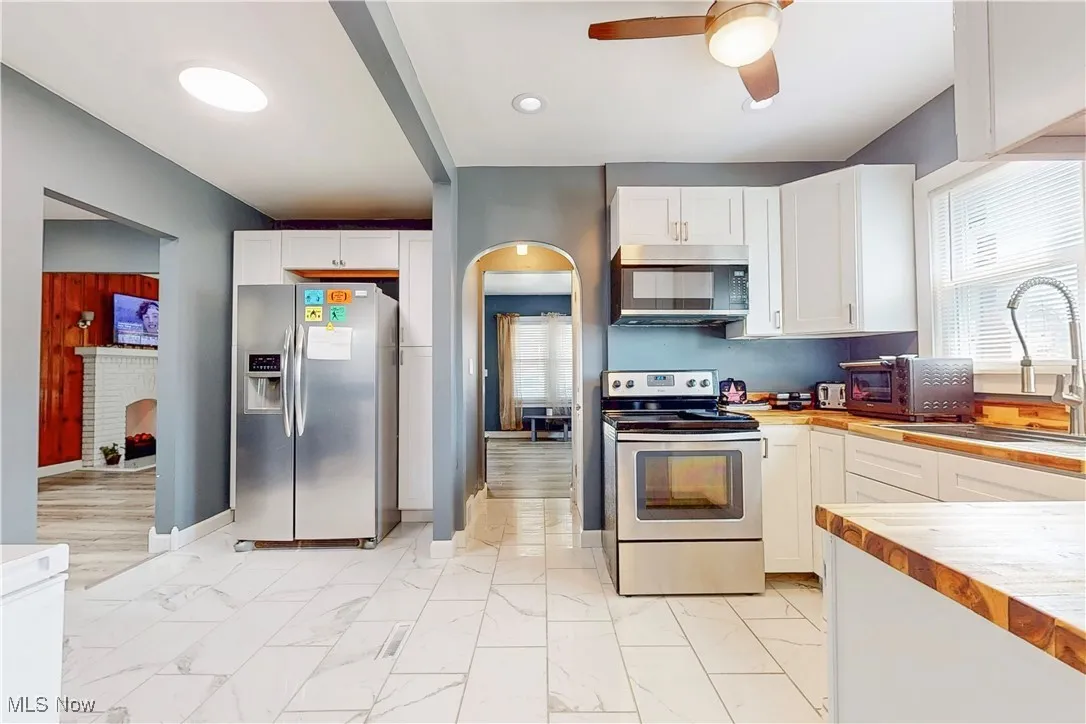 Kitchen featuring stainless steel appliances, light marble finish flooring, white cabinetry, a ceiling fan, and arched walkways