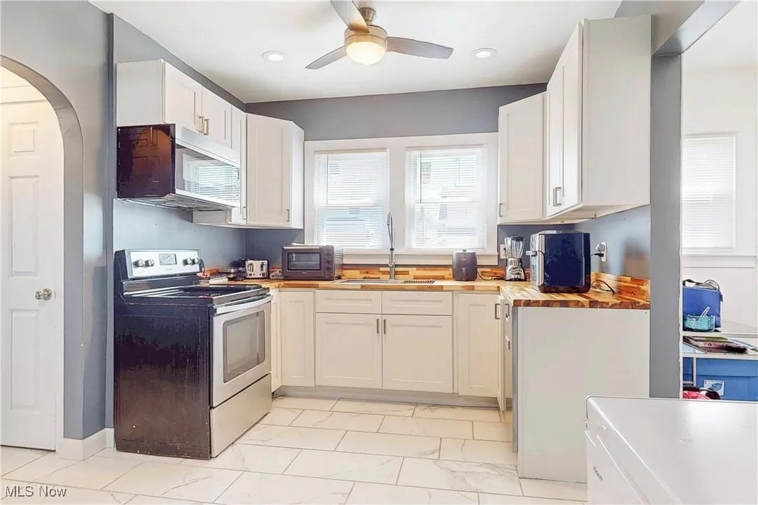 Kitchen with stainless steel range with electric cooktop, ceiling fan, light marble finish flooring, arched walkways, and white cabinets