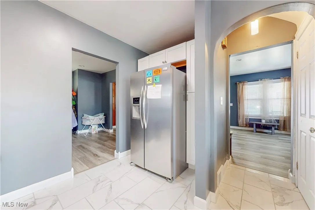 Kitchen with stainless steel fridge with ice dispenser, light marble finish floors, white cabinetry, and arched walkways