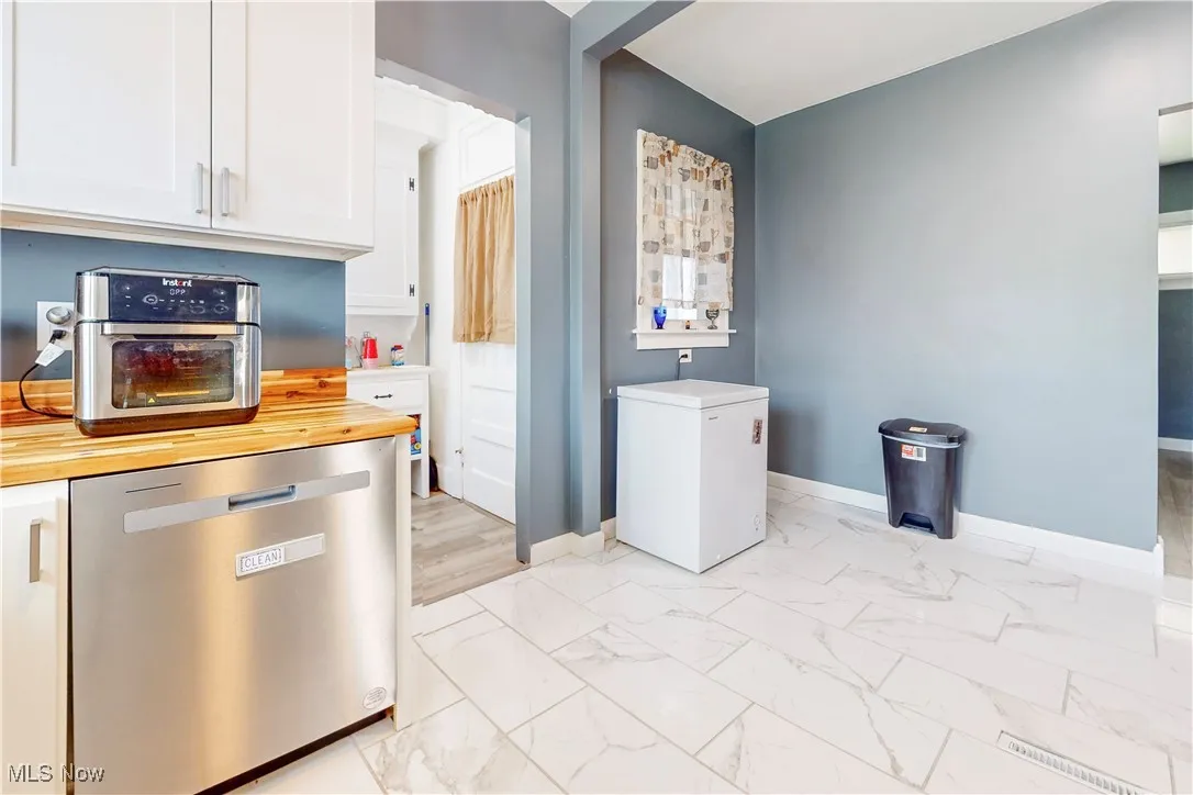 Kitchen featuring dishwasher, wooden counters, light marble finish floors, refrigerator, and white cabinets
