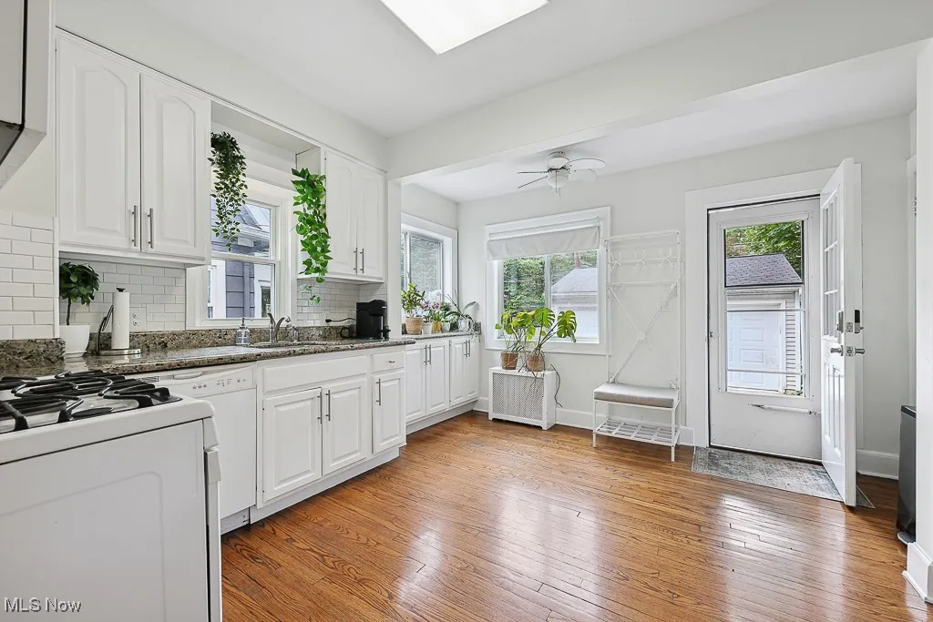Kitchen featuring white appliances, backsplash, light wood-style flooring, white cabinets, and radiator heating unit