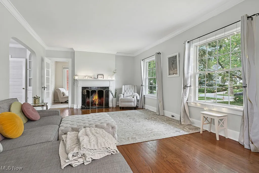 Living area featuring hardwood / wood-style flooring, ornamental molding, arched walkways, and a warm lit fireplace