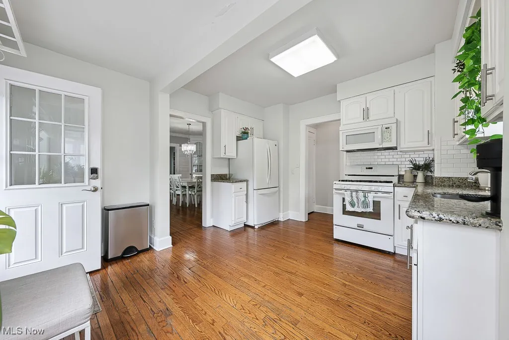 Kitchen with white appliances, white cabinets, hardwood / wood-style flooring, and dark stone countertops