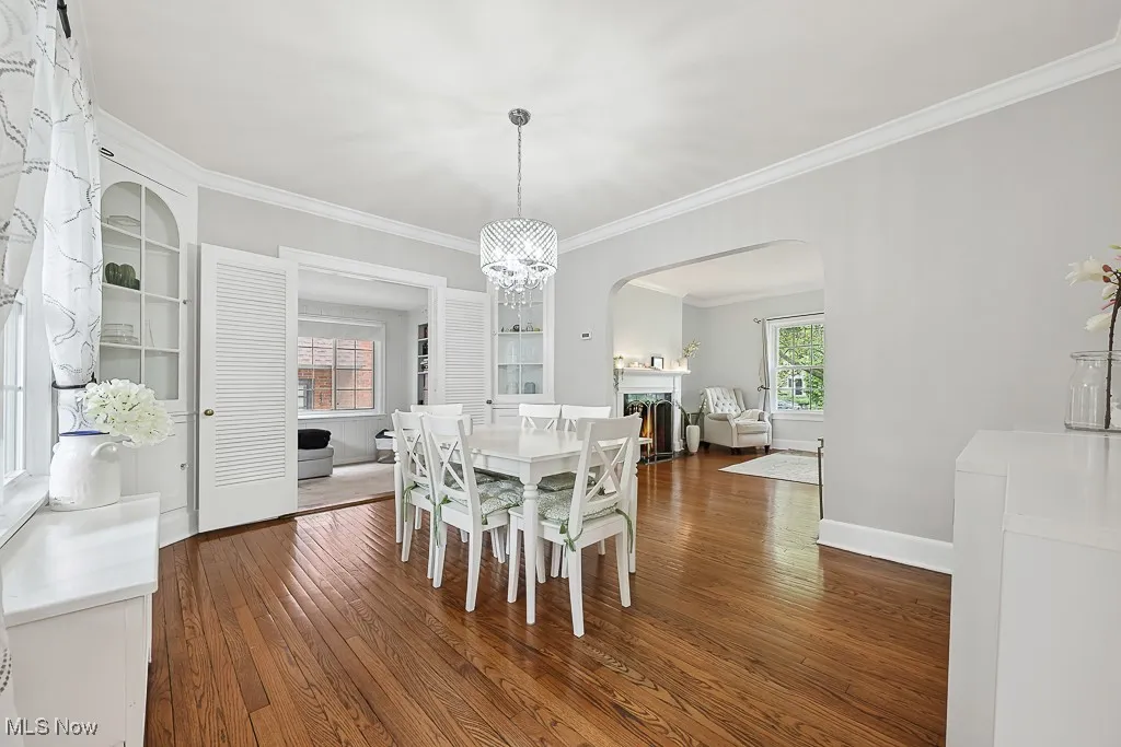 Dining area featuring ornamental molding, wood-type flooring, arched walkways, and a warm lit fireplace