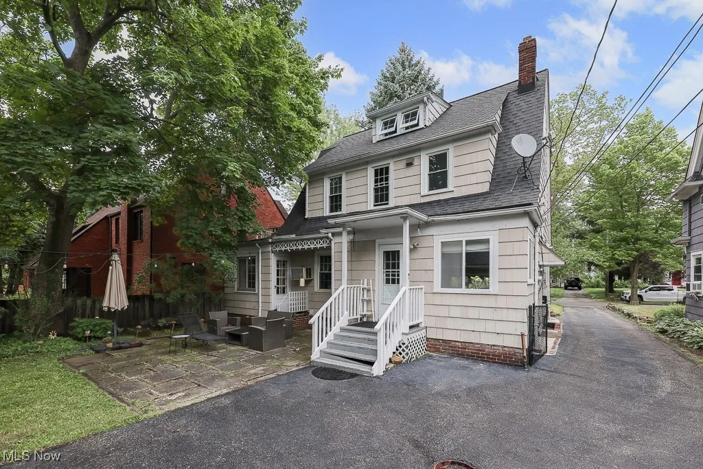 View of front facade featuring a chimney, roof with shingles, and a patio