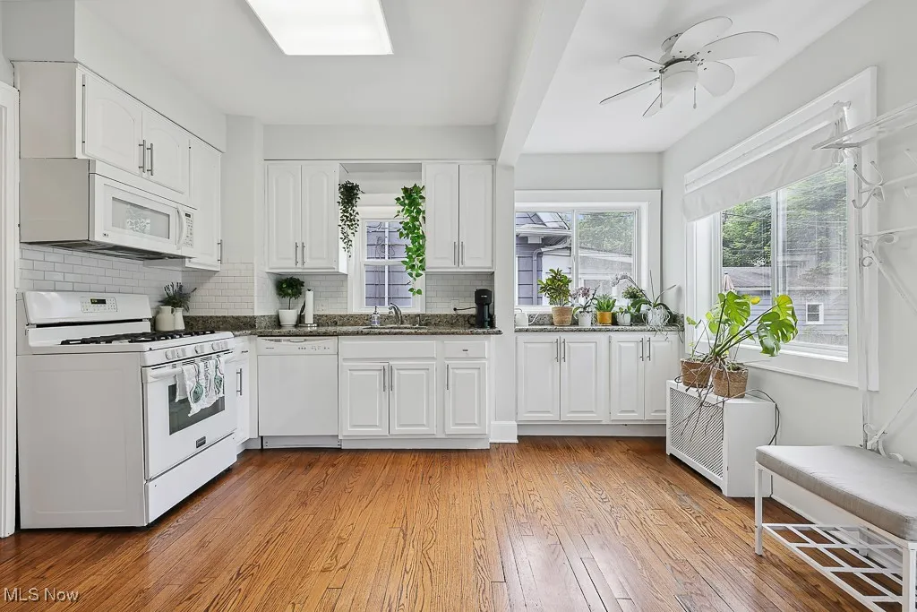 Kitchen featuring white appliances, white cabinetry, light wood finished floors, decorative backsplash, and dark stone counters