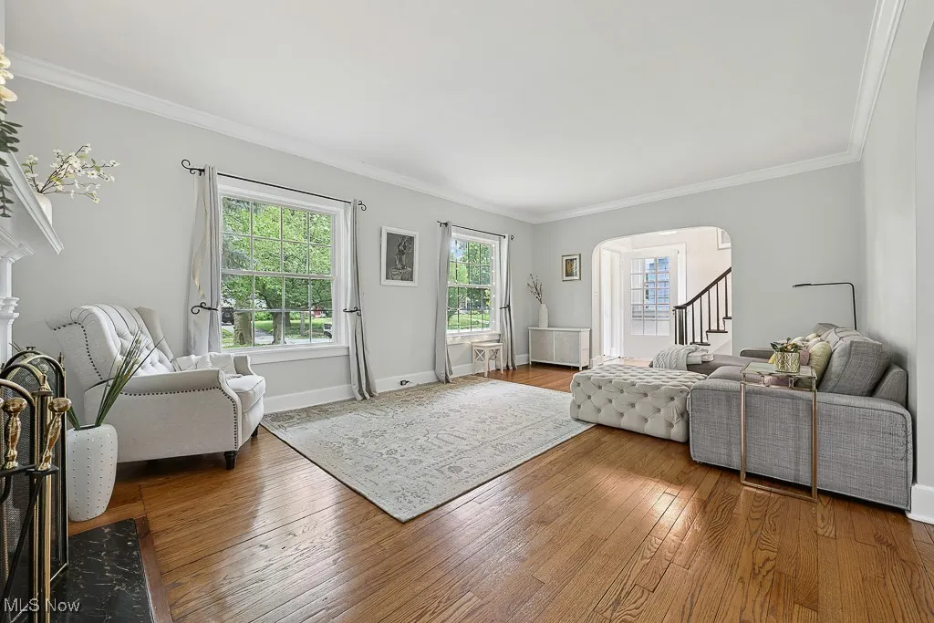 Living area featuring arched walkways, crown molding, wood-type flooring, radiator heating unit, and stairs