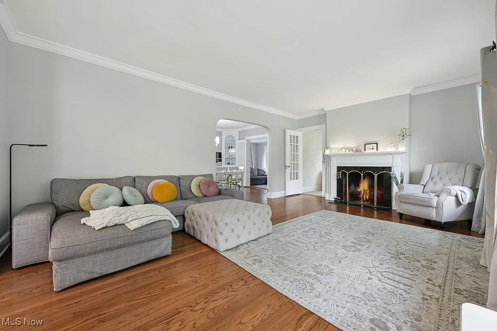 Living room with arched walkways, wood finished floors, crown molding, and a warm lit fireplace