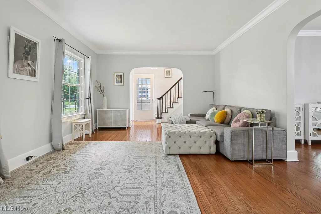 Living room with arched walkways, crown molding, wood finished floors, radiator heating unit, and stairway
