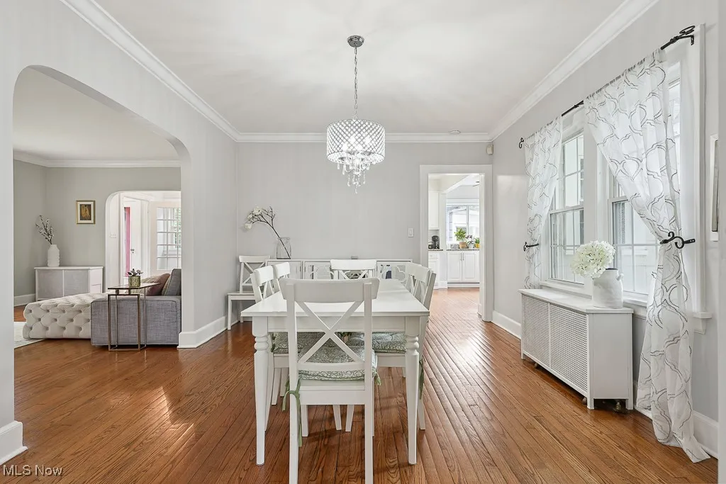 Dining space with arched walkways, radiator heating unit, crown molding, a chandelier, and hardwood / wood-style floors