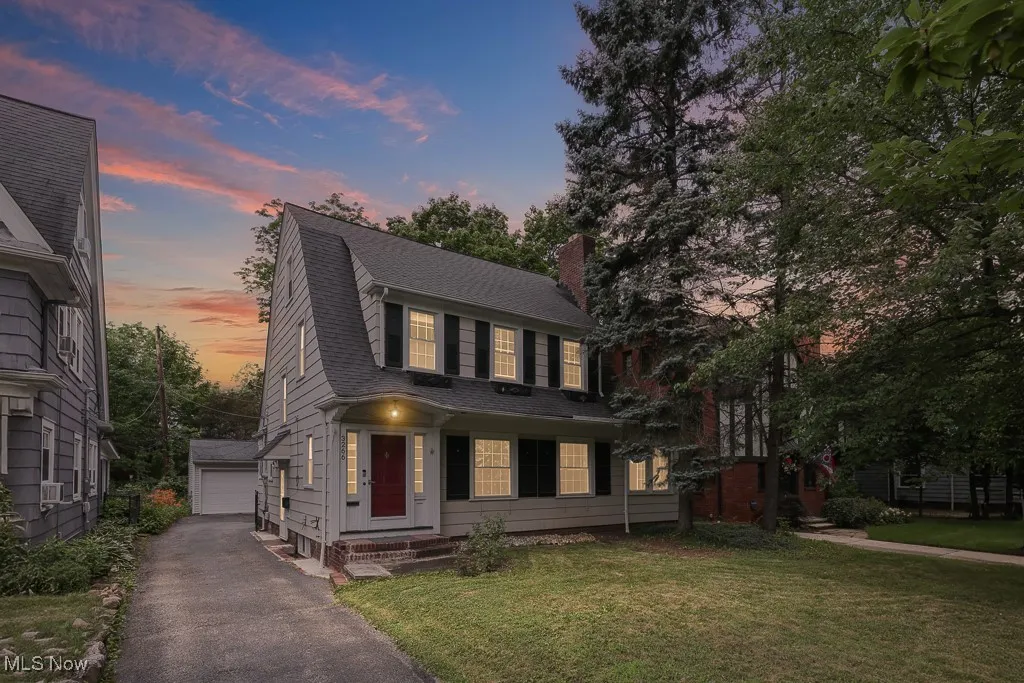 View of front facade featuring an outbuilding, a gambrel roof, a shingled roof, a lawn, and a chimney