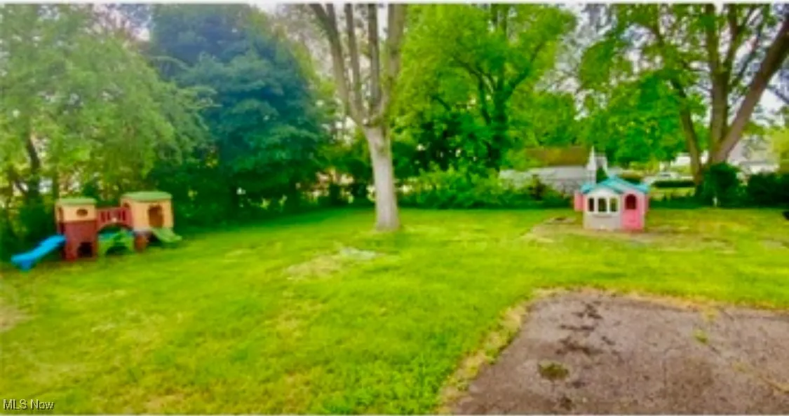 View of green lawn with a playground and view of scattered trees