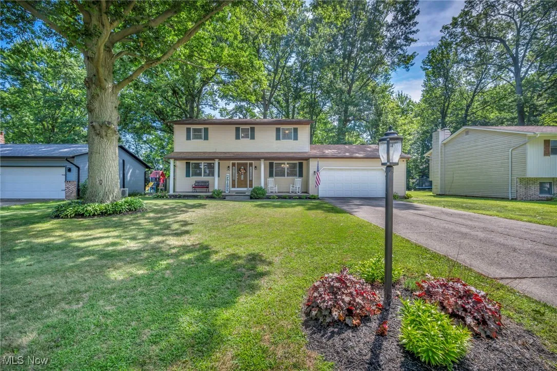 Traditional home with a porch, driveway, an attached garage, and a front yard