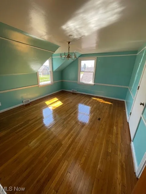 Additional living space featuring healthy amount of natural light, hardwood / wood-style floors, lofted ceiling, and a chandelier