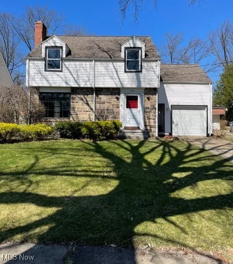View of front facade featuring a garage, a chimney, stone siding, and a front yard