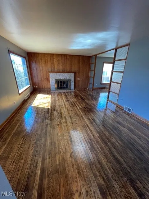 Unfurnished living room featuring dark wood finished floors, a glass covered fireplace, and wood walls