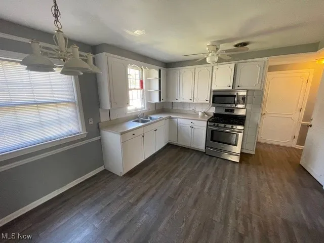 Kitchen with stainless steel appliances, dark wood-style flooring, white cabinets, and ceiling fan