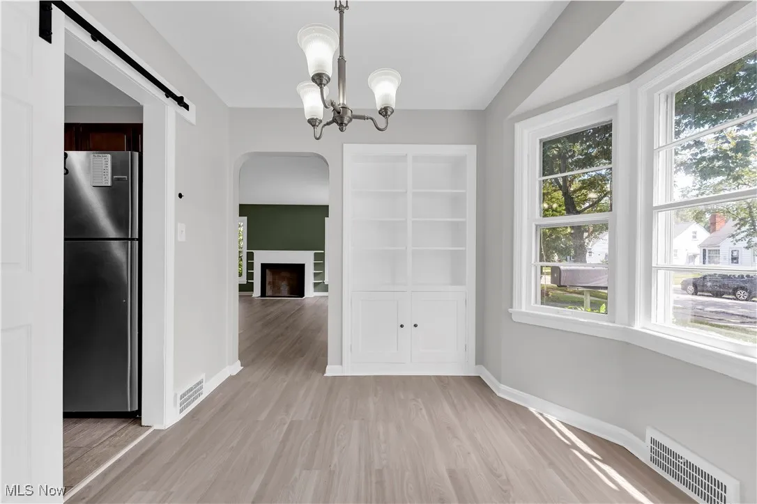 Unfurnished dining area featuring arched walkways, light wood-style floors, built in shelves, a chandelier, and a barn door