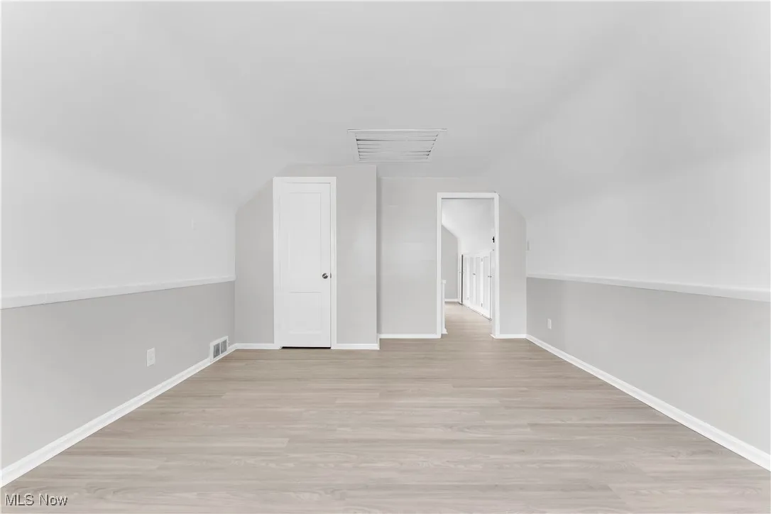 Additional living space with light wood finished floors and vaulted ceiling