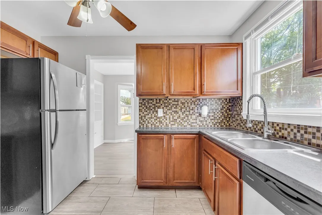 Kitchen featuring stainless steel appliances, a ceiling fan, brown cabinetry, and decorative backsplash