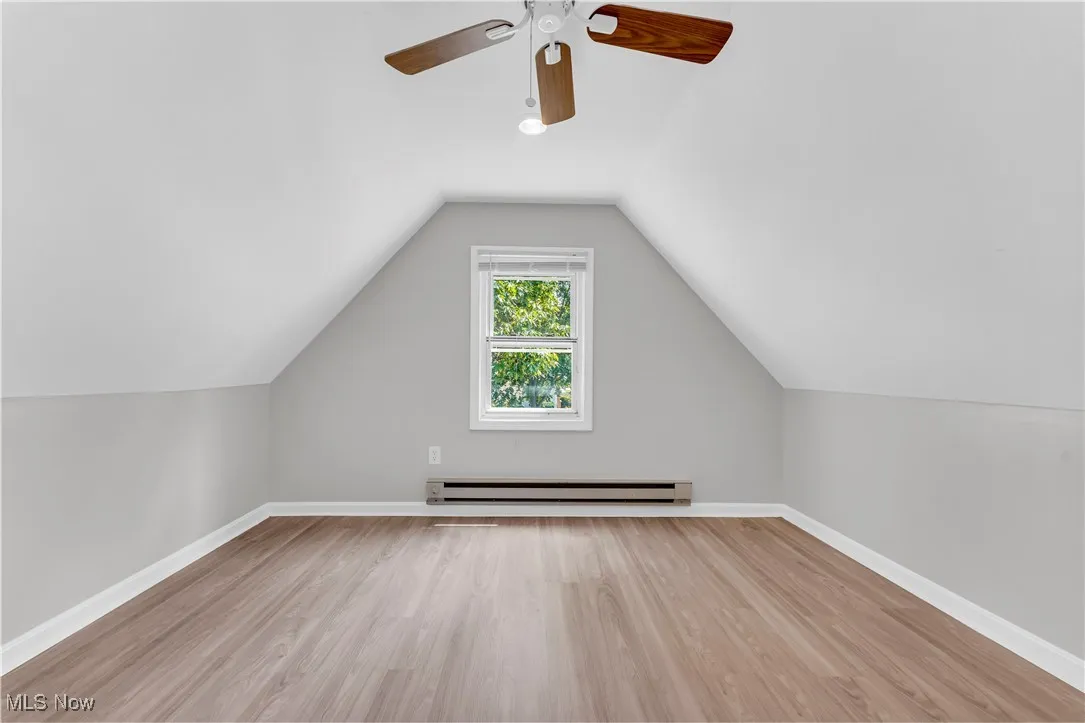 Additional living space with wood finished floors, vaulted ceiling, ceiling fan, and a baseboard heating unit