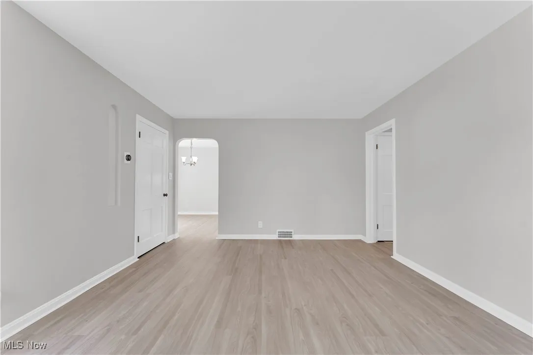Empty room featuring light wood finished floors, arched walkways, and a chandelier