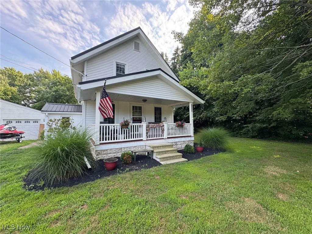 View of front facade with a porch, a front lawn, a metal roof, and a garage