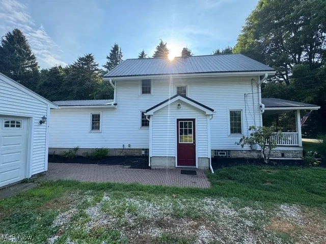 Side of house with a metal roof, a lawn, covered porch, and a garage