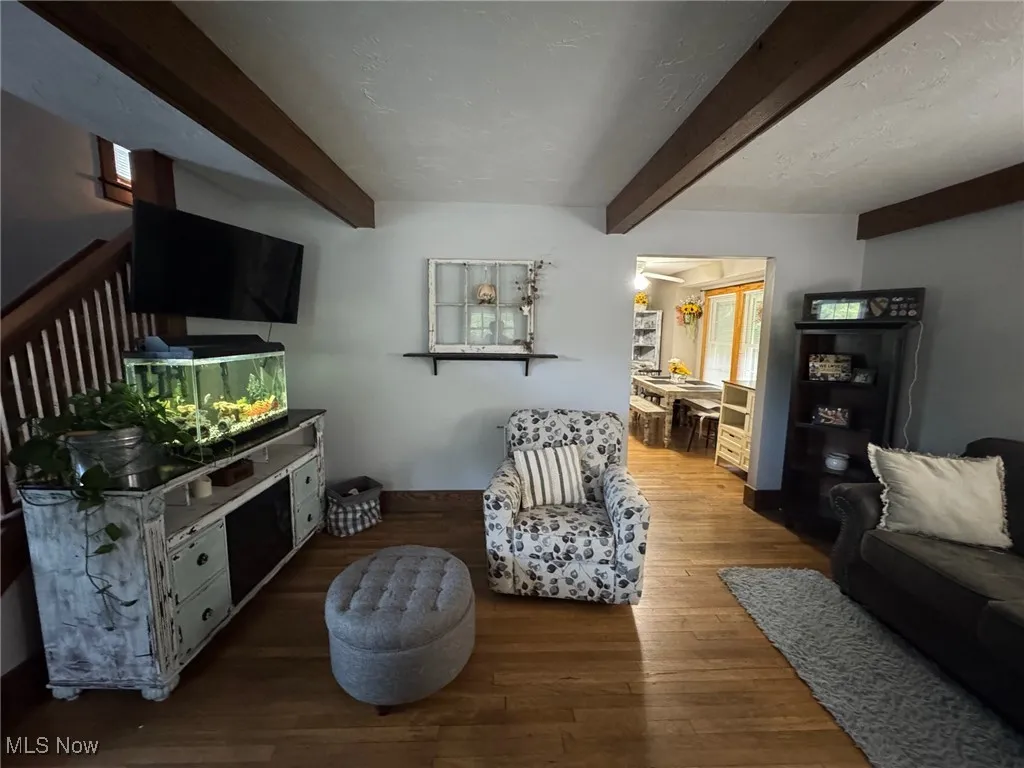 Living room with beam ceiling, wood-type flooring, and stairs