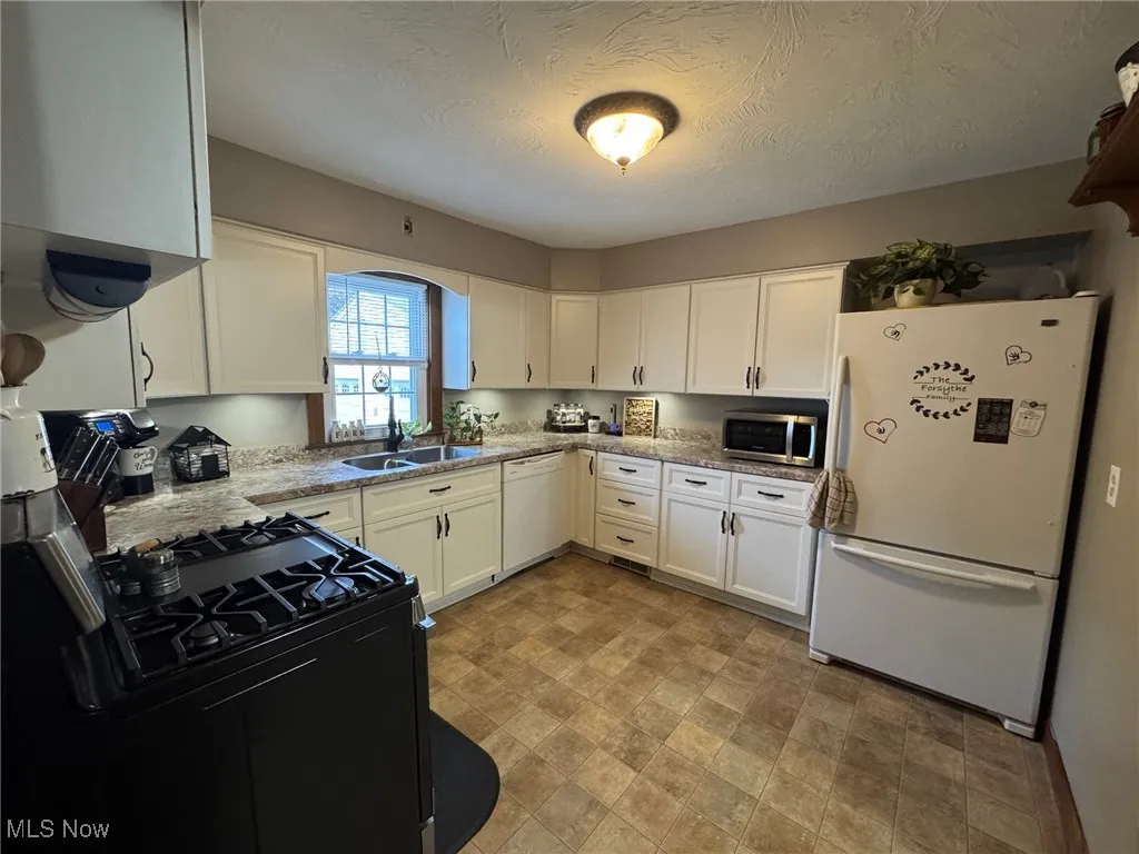 Kitchen with white cabinets, a textured ceiling and all appliances