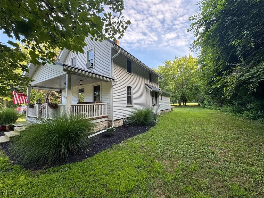 View of side of home featuring a porch and a lawn