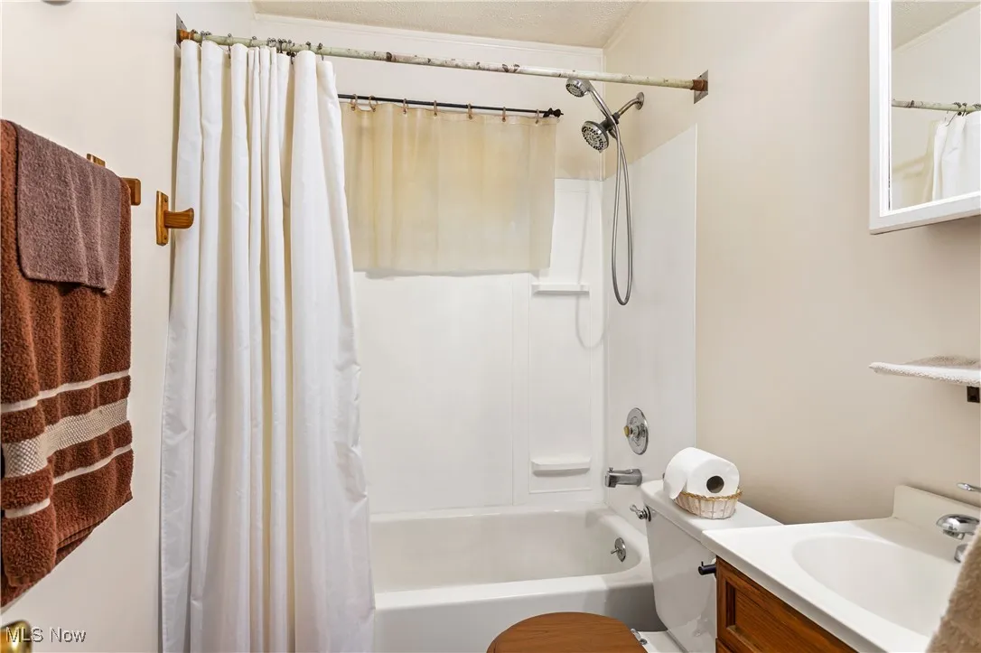 Bathroom with shower / bath combo, vanity, ornamental molding, and a textured ceiling