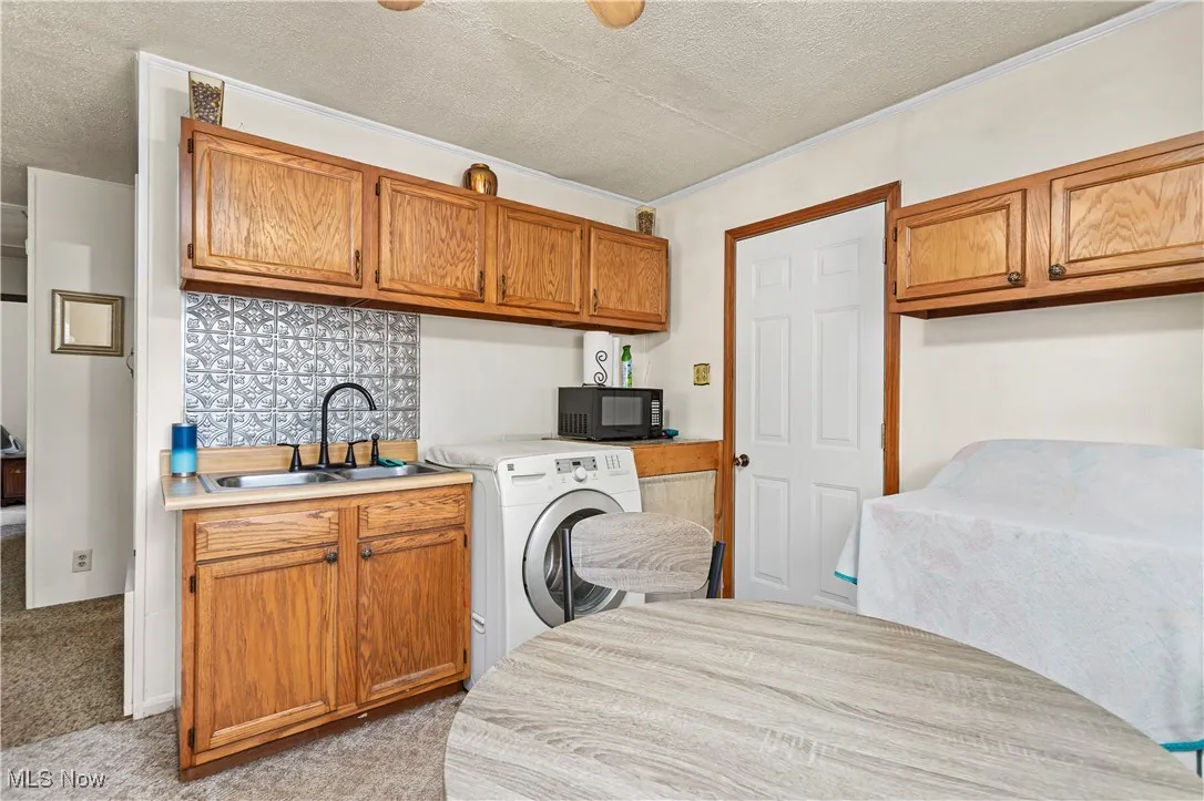 Kitchen featuring black microwave, a textured ceiling, washer / dryer, brown cabinets, and light countertops