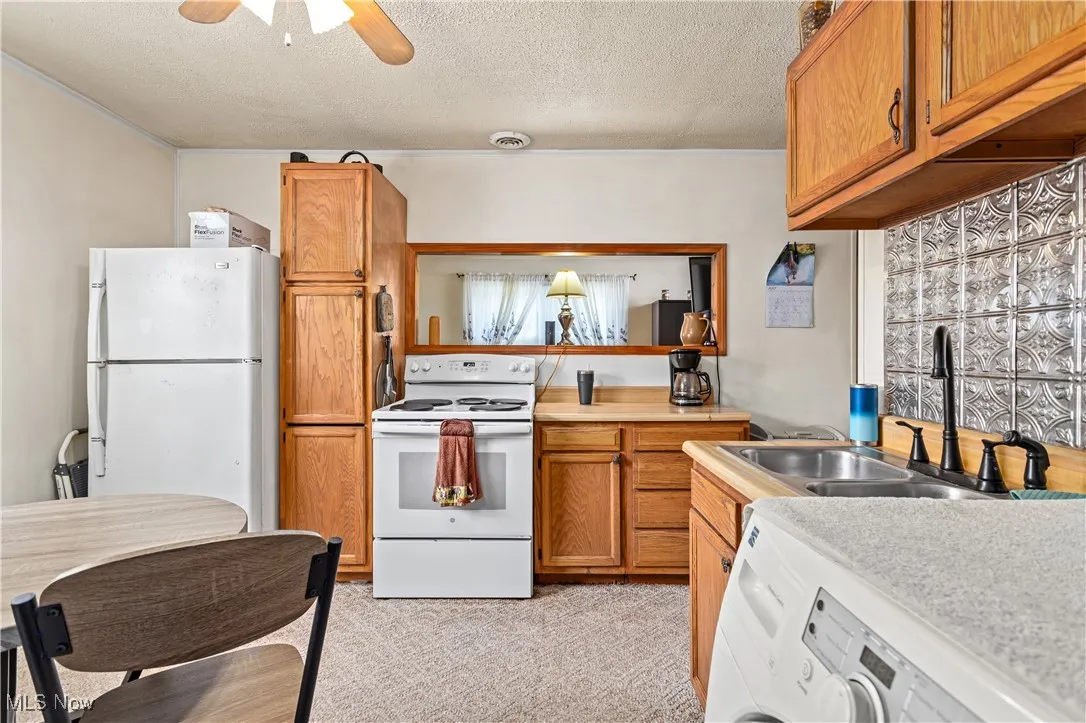 Kitchen featuring white appliances, a textured ceiling, washer / clothes dryer, brown cabinets, and ceiling fan
